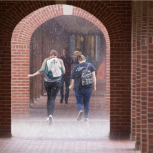 Students running in the rain through brick archways