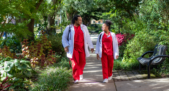 Two BC nursing students walking underneath a canopy of oak trees on campus