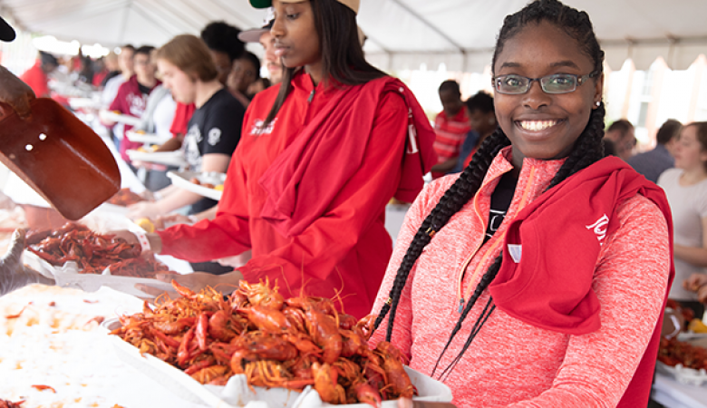 BC student in a red pullover holding a tray of crawfish at Lagniappe Day