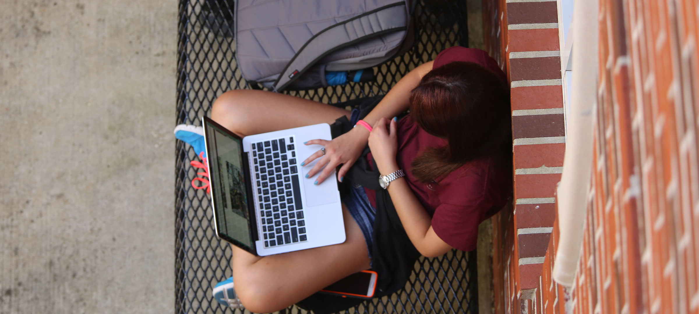 Bryman College student sits on campus and looks at her laptop while leaning against a brick wall